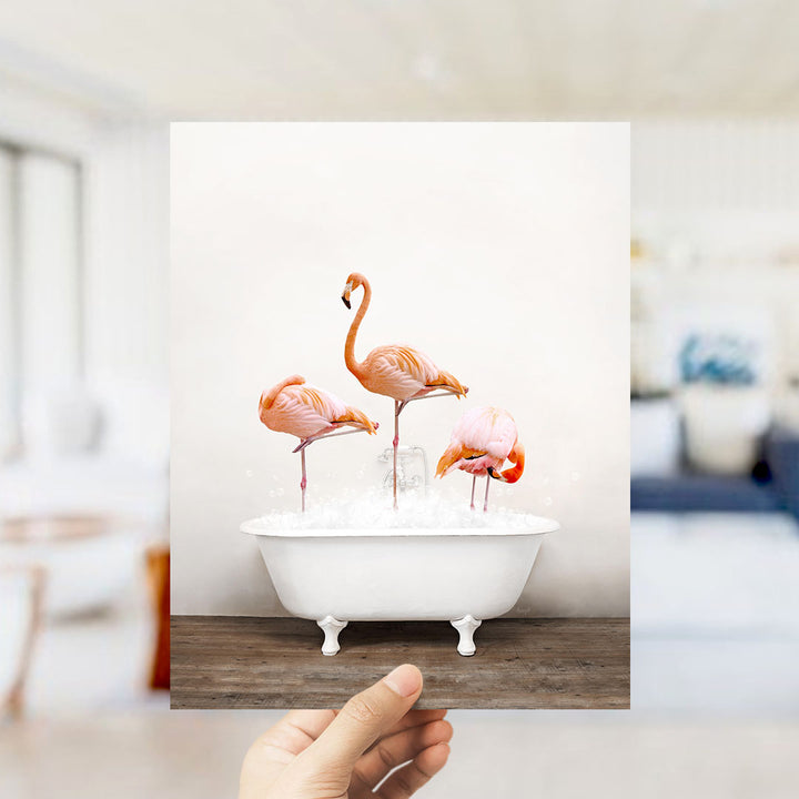 A hand holds up a photograph of three pink flamingos standing in a white bathtub filled with water.