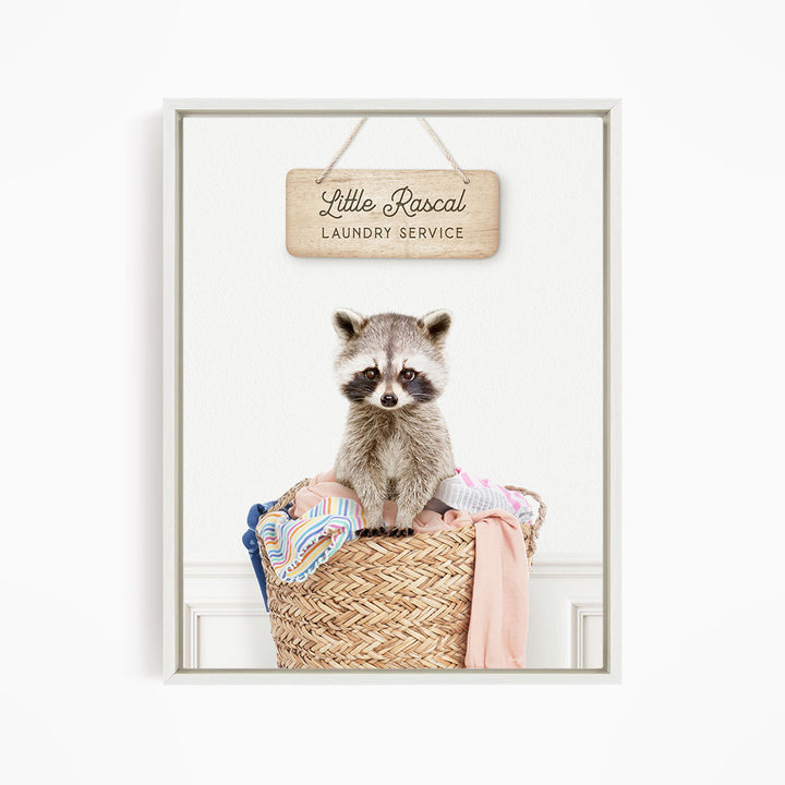 A raccoon sitting in a woven laundry basket, with a sign above that reads "Little Racal Laundry Service".