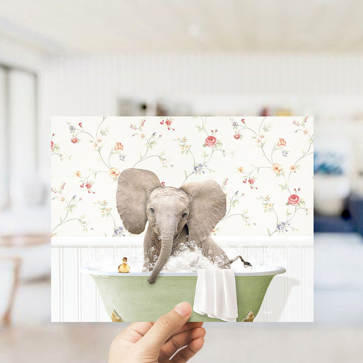 A hand holds up a collage of two images: an elephant sitting in a bathtub with a floral wallpaper backdrop, and a small bird sitting on the edge of the tub.