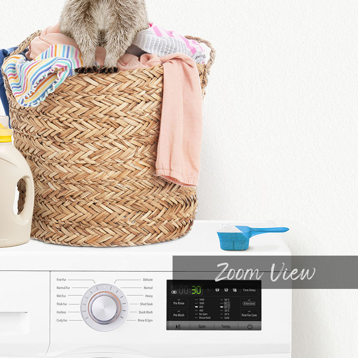 A laundry basket filled with clothes sits on top of a washing machine, with a blue measuring cup and a white bottle nearby.