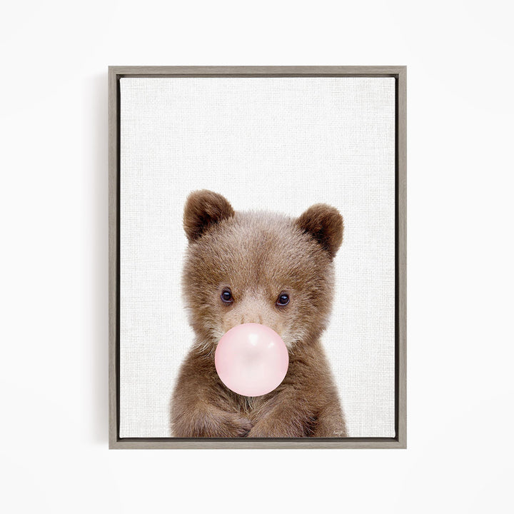 A cute brown bear is blowing a bubble with a pink bubble gum bubble.