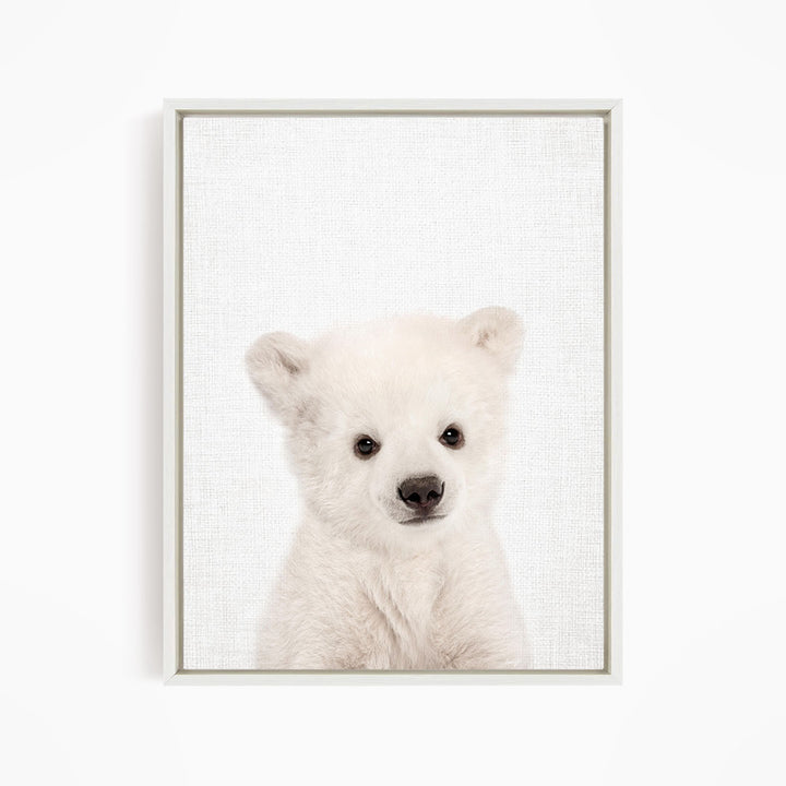 A cute white polar bear cub with large eyes and a black nose is the focus of the image.