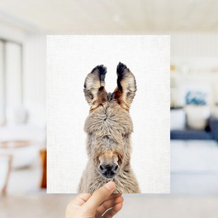 A hand is holding up a square print of a donkey's head, showing its fluffy ears and nose.