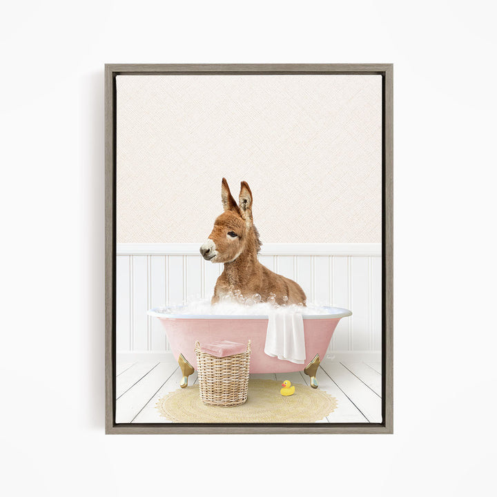 A donkey is sitting in a pink bathtub filled with water, surrounded by a yellow rubber duck and a basket.