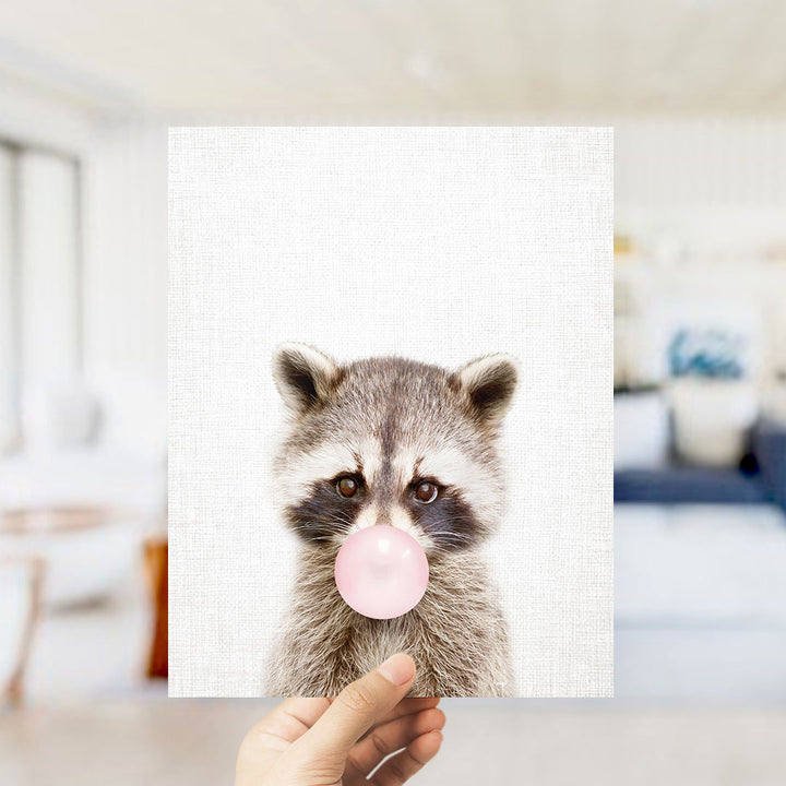 A raccoon blowing a bubble with a pink bubble gum bubble.