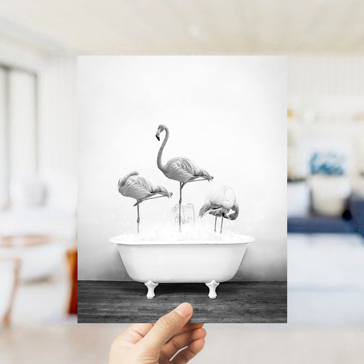 A hand holds up a black and white photograph of three flamingos standing in a bathtub filled with water.
