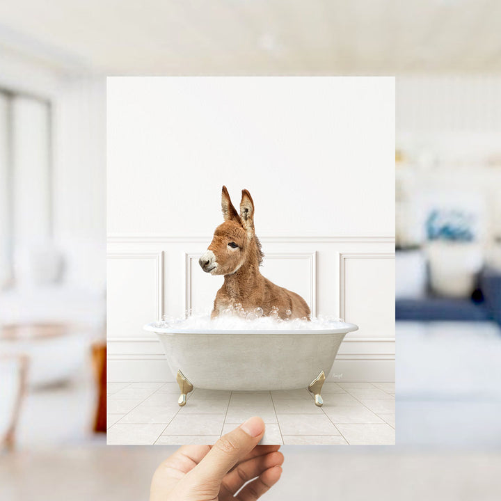 A donkey sitting in a bathtub filled with bubbles, with a person's hand holding up the image.