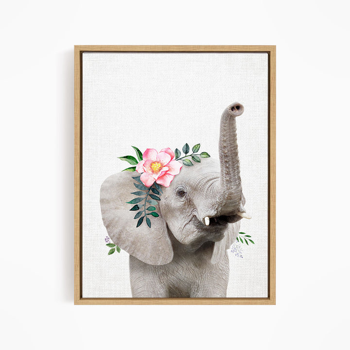 A framed print of an elephant with a pink flower on its ear and green leaves around its trunk.