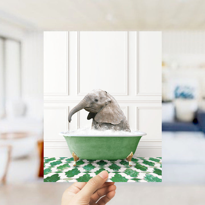 A small elephant is sitting in a green bathtub filled with water, surrounded by a patterned green and white floor.