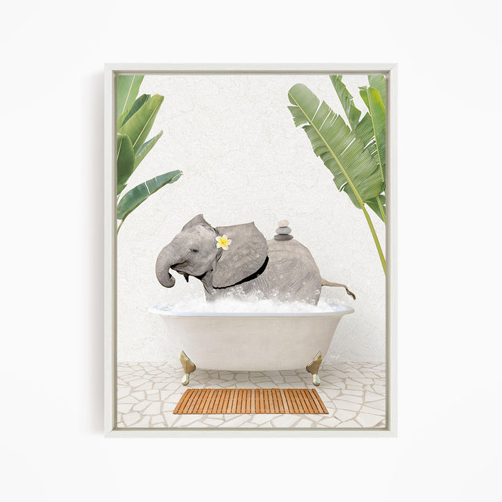 A gray elephant is sitting in a white bathtub filled with water, surrounded by green leaves and a wooden mat on the floor.