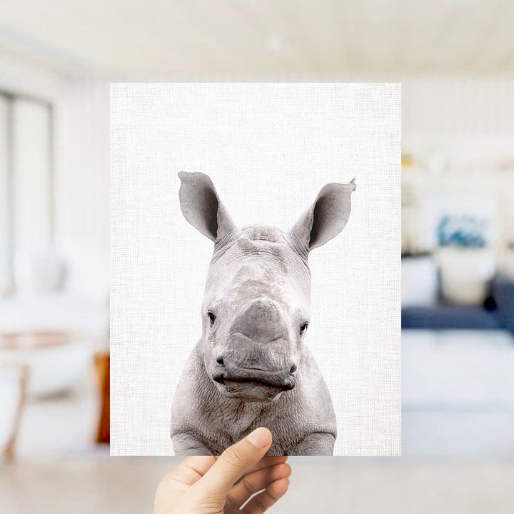 A hand is holding up a framed image of a rhinoceros, which is the main focus of the image.