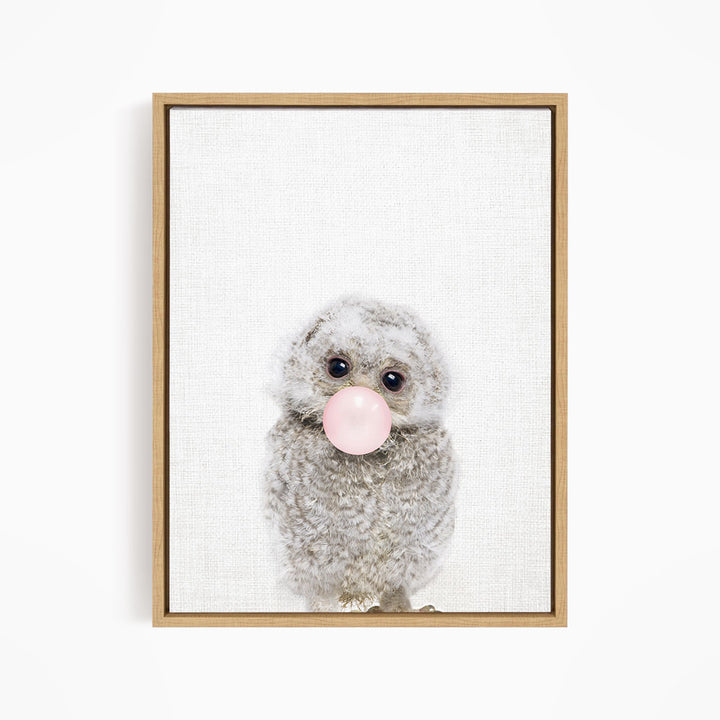 A fluffy gray owl is blowing a pink bubble with its beak, creating a whimsical and playful scene.