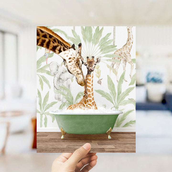 A hand holds up a framed image depicting a giraffe and a baby giraffe in a bathtub, surrounded by tropical foliage.
