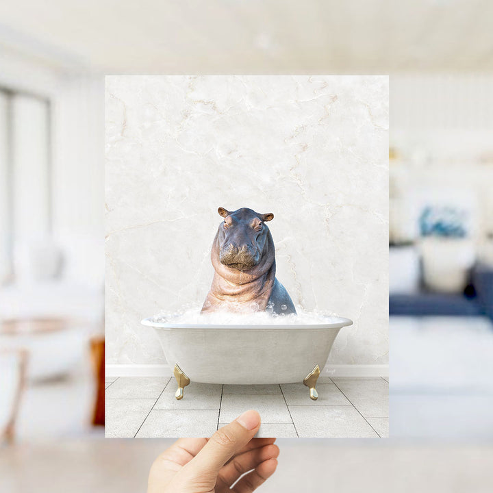 A hand holds up a framed image of a hippopotamus sitting in a bathtub filled with water, creating a whimsical and playful scene.