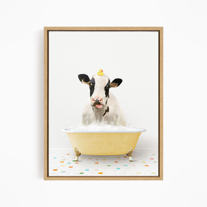 A black and white cow is sitting in a yellow bathtub filled with bubbles, with a rubber duck perched on its head.