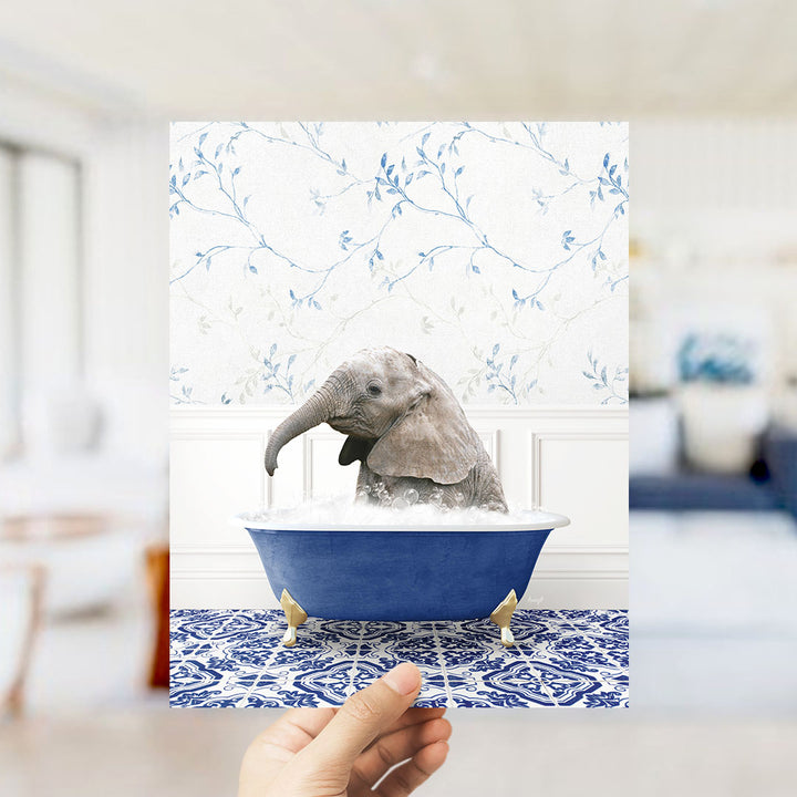 A small elephant is sitting in a blue bathtub filled with water, surrounded by a patterned blue and white rug.