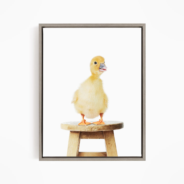 A small yellow duck standing on a wooden stool.