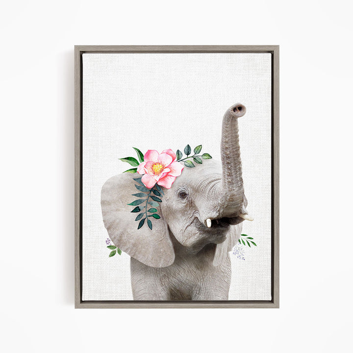 A gray elephant with a pink flower on its ear and green leaves around its trunk is the main subject of the framed artwork.
