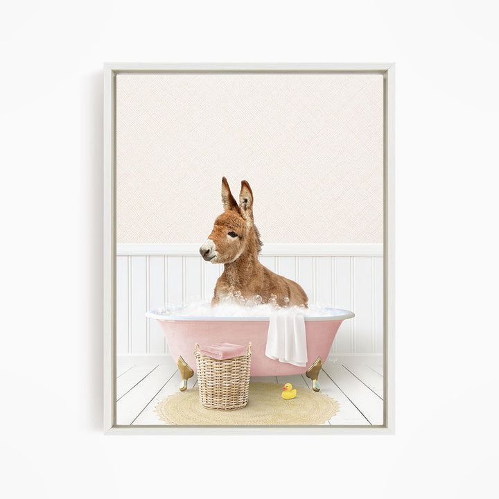 A donkey is sitting in a pink bathtub filled with water, surrounded by a yellow rubber duck and a basket.