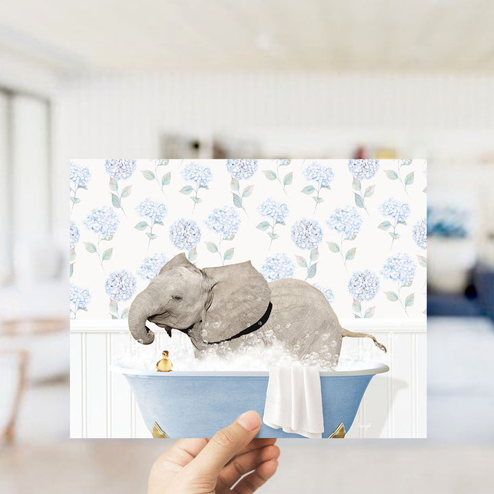A hand holds up a print featuring an elephant taking a bath in a blue tub, surrounded by a floral pattern.