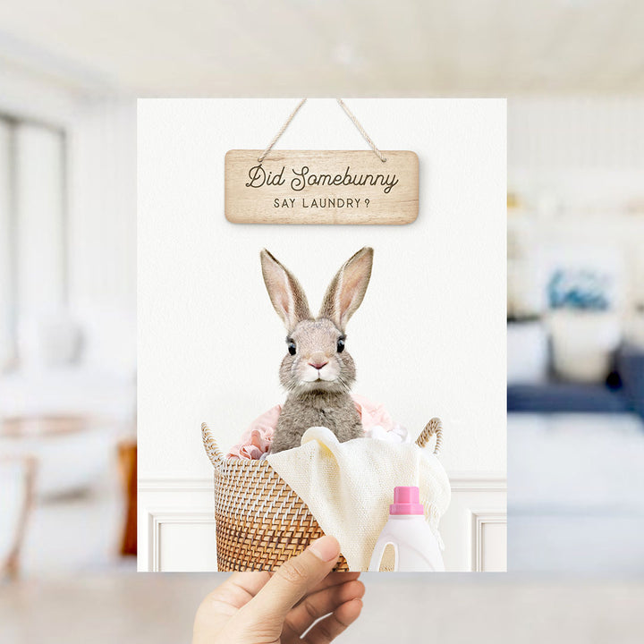 A hand holding a sign that says "Did Somebunny Say Laundry?" with a picture of a rabbit sitting in a basket of laundry.