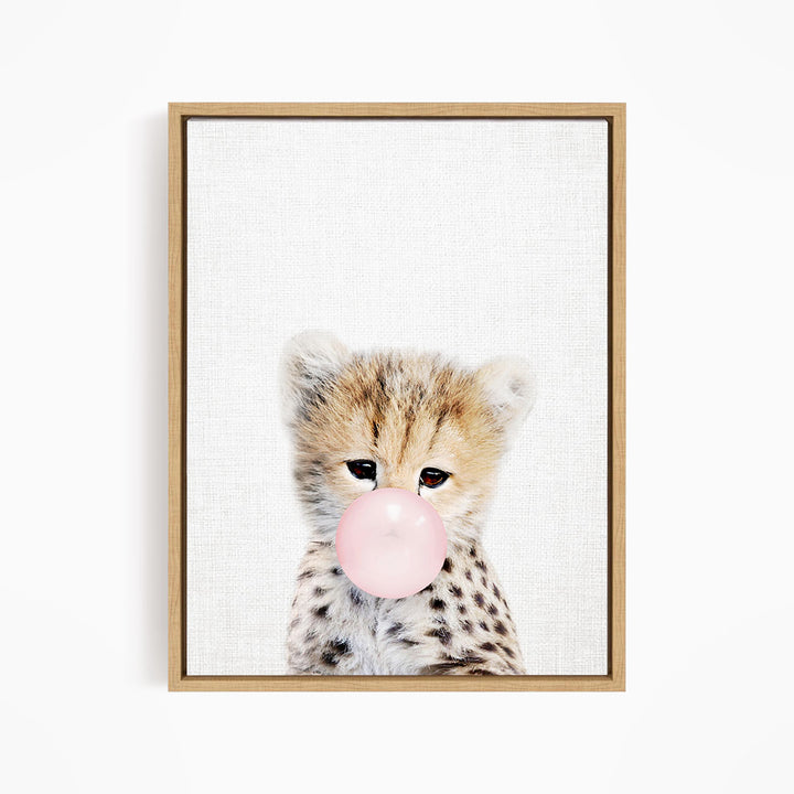 A young cheetah with spotted fur blowing a bubble with a pink bubble gum bubble.