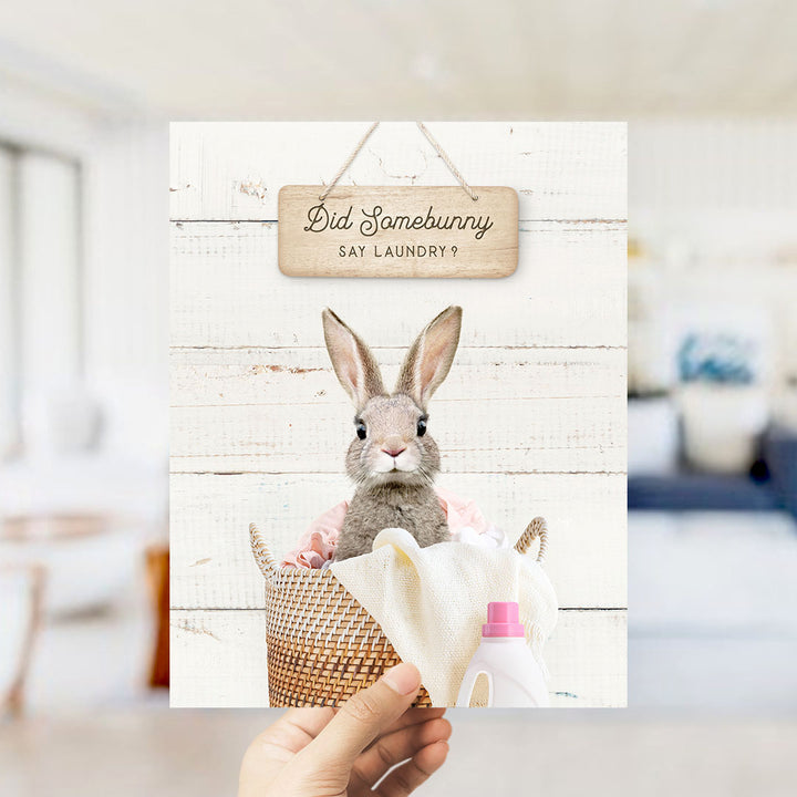 A hand holding a card with a picture of a rabbit sitting in a basket, with a sign above it that says "Did Somebunny Say Laundry?".