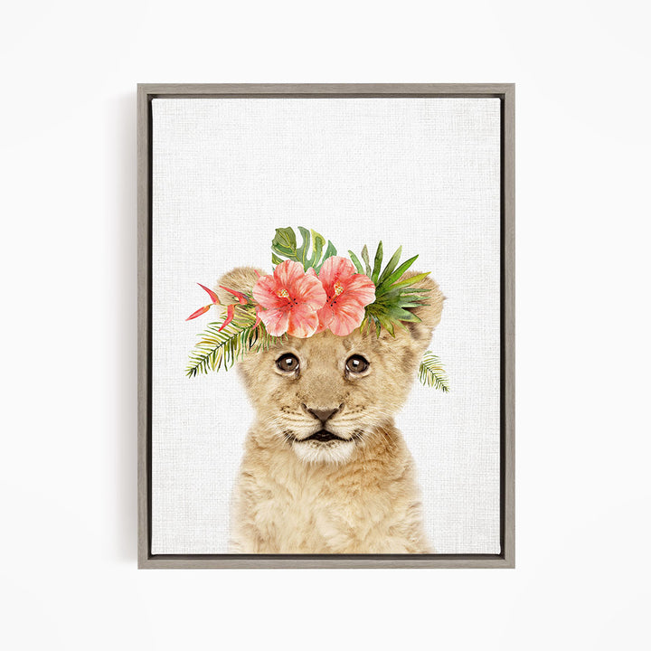 A young lion cub wearing a floral headpiece with pink and red flowers and green leaves.