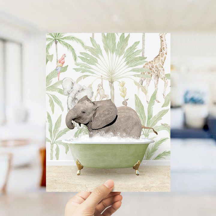 A hand holds up a framed print featuring an illustration of an elephant bathing in a green bathtub, surrounded by tropical foliage and animals.