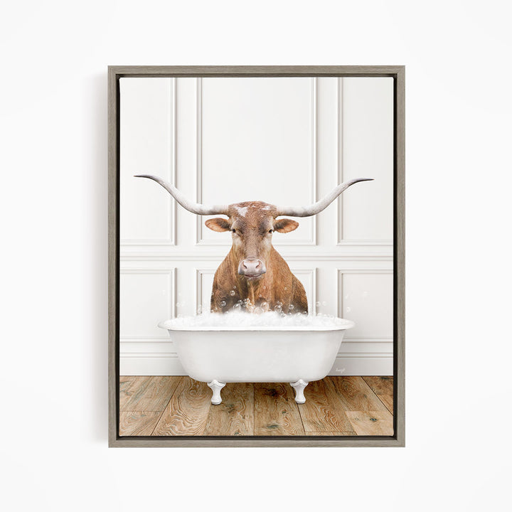 A brown steer with large horns is sitting in a white bathtub, surrounded by bubbles, in a white-walled room.