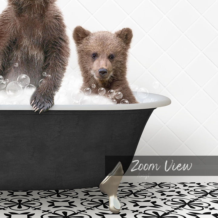 A young bear cub sitting in a bathtub filled with bubbles, with a black bathtub and a patterned tile floor visible in the image.