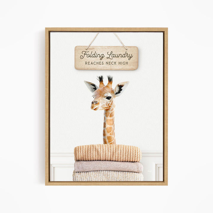 A giraffe standing on a pile of folded clothes, with a wooden sign above that says "Folding Laundry Reaches Neck High".