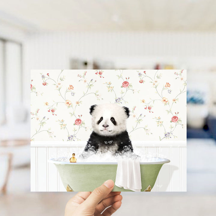 A hand holding a framed image of a panda bear sitting in a bathtub filled with bubbles, with a floral wallpaper in the background.