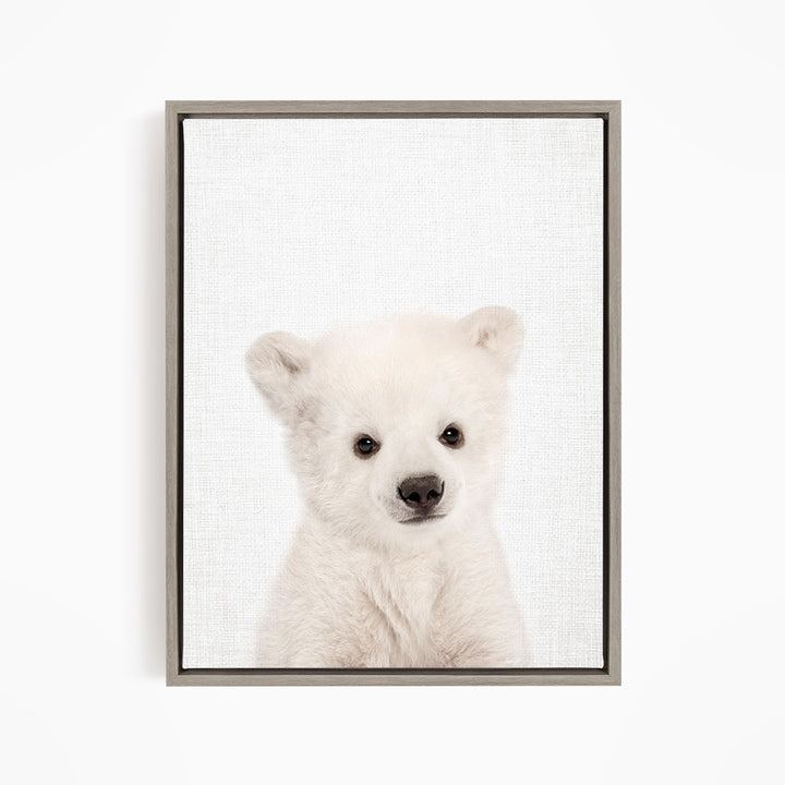 A cute white polar bear cub with large eyes and a black nose is the focus of the image.