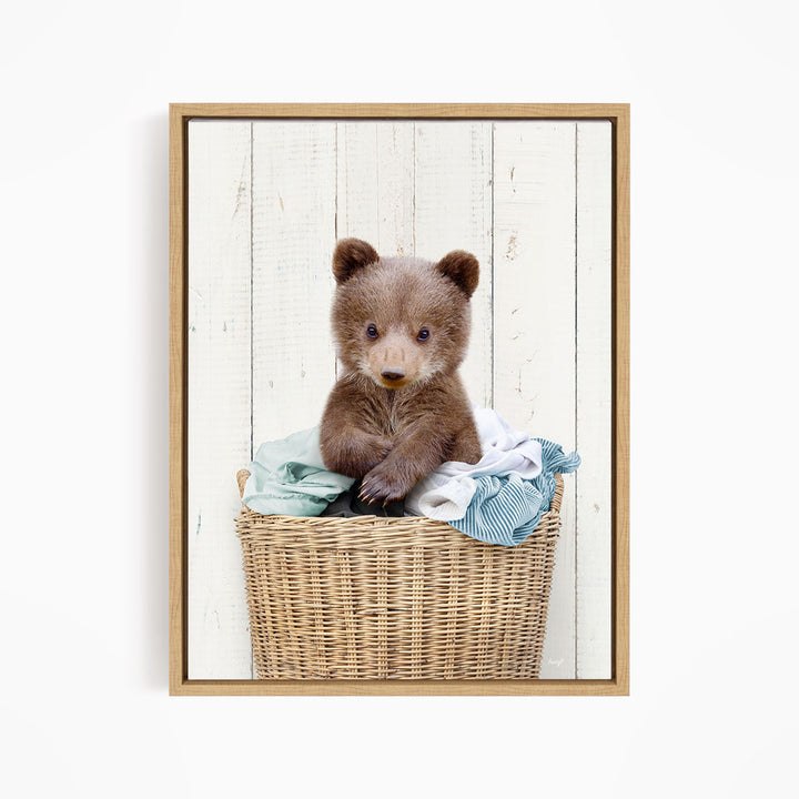 A cute brown bear cub sitting in a wicker basket filled with clothes.