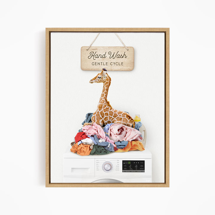 A giraffe sitting on a pile of laundry inside a washing machine, with a sign above that says "Hand Wash Gentle Cycle".