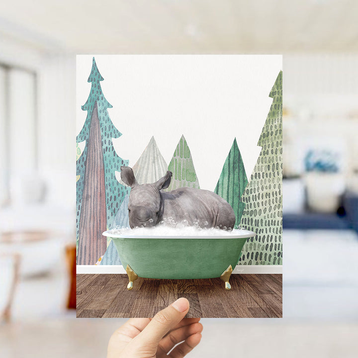 A hand holds up a collage of an image featuring a rhinoceros sitting in a green bathtub, surrounded by stylized trees and a snowy landscape.