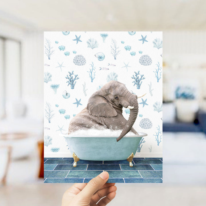 A hand is holding up a framed image of an elephant sitting in a bathtub filled with bubbles, surrounded by a blue and white ocean-themed background.