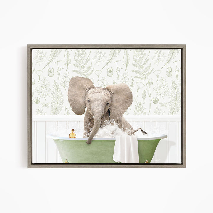 A baby elephant sitting in a green bathtub filled with bubbles, surrounded by a white wall with a pattern of leaves and ferns.