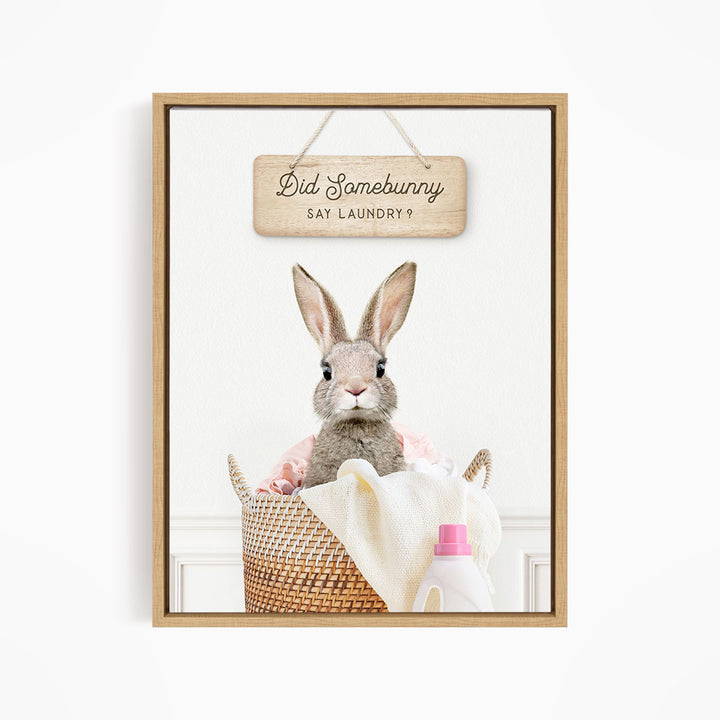 A cute rabbit sitting in a woven basket filled with laundry, with a sign above that says "Did Somebunny Sat Laundry?".
