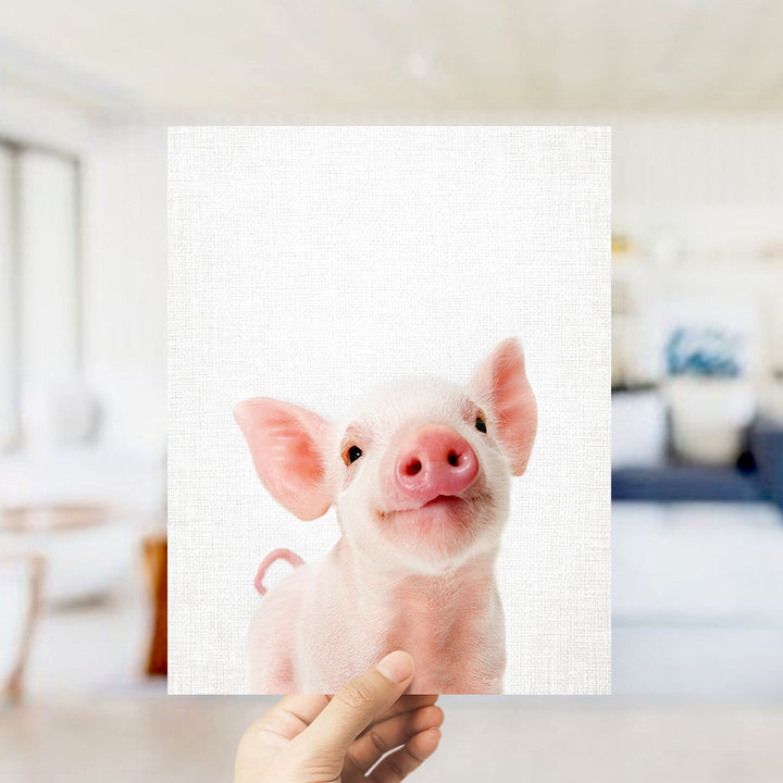 A hand is holding up a square image of a cute, pink pig with a big smile on its face.