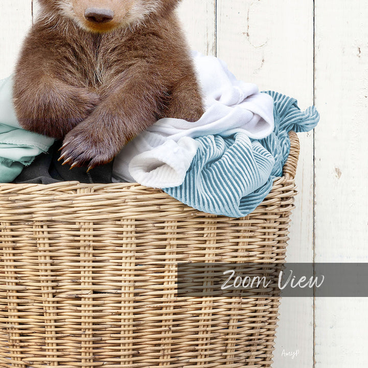 A brown bear sitting in a wicker basket filled with clothes.