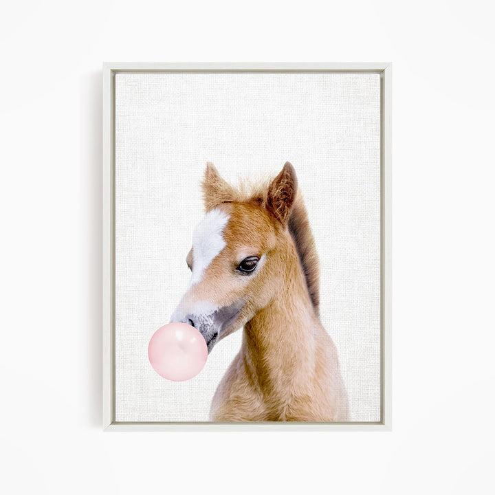 A young horse blowing a bubble with a pink bubble gum bubble.