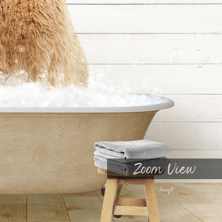 A fluffy brown cat is sitting in a bathtub filled with bubbles, with a wooden stool and towels nearby.
