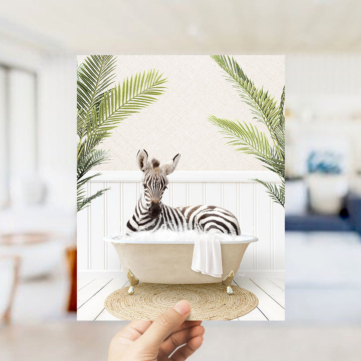 A zebra lying in a bathtub surrounded by palm leaves, with a hand holding the image up to the camera.