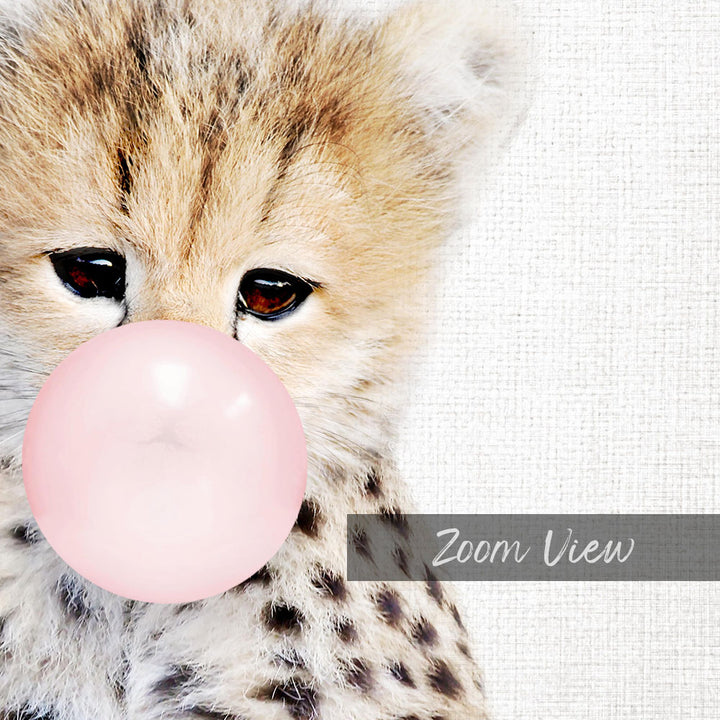 A close-up of a cheetah cub blowing a bubble with a pink bubble gum bubble, with a white background.