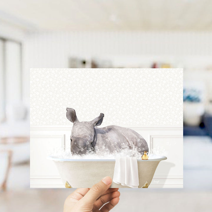 A rhinoceros is sitting in a bathtub filled with bubbles, surrounded by a towel and a small yellow duck.