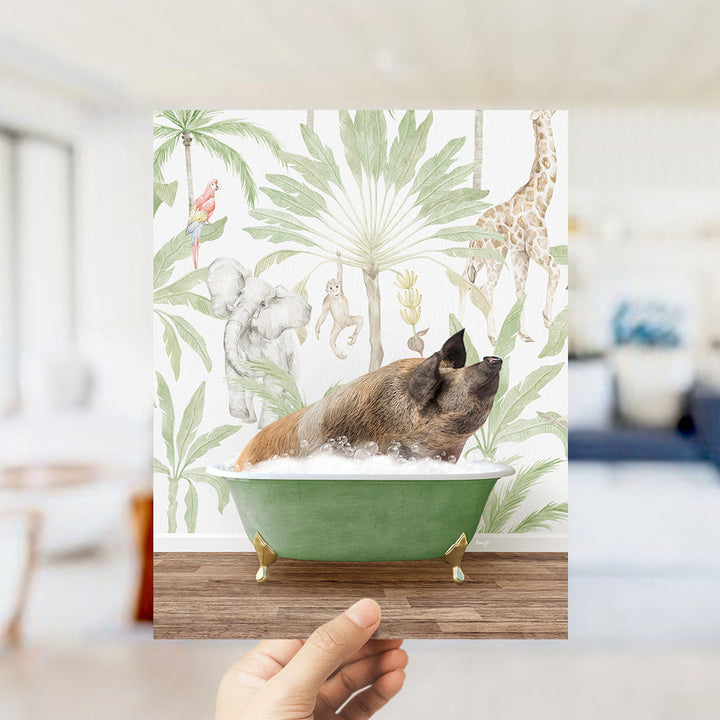 A hand holds up a framed print featuring a whimsical illustration of a pig sitting in a bathtub surrounded by tropical foliage, including a giraffe and other animals.