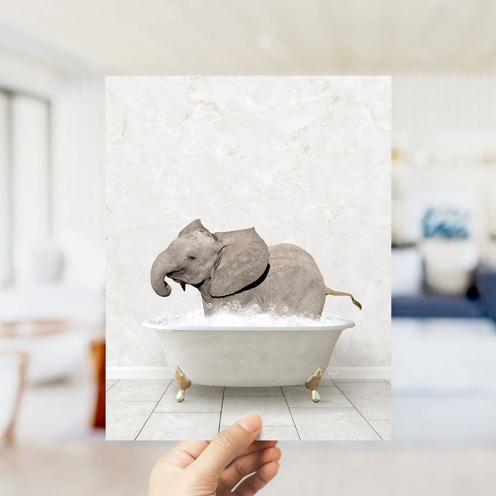 A hand holds up a framed image of a baby elephant sitting in a bathtub filled with water, creating a whimsical and playful scene.