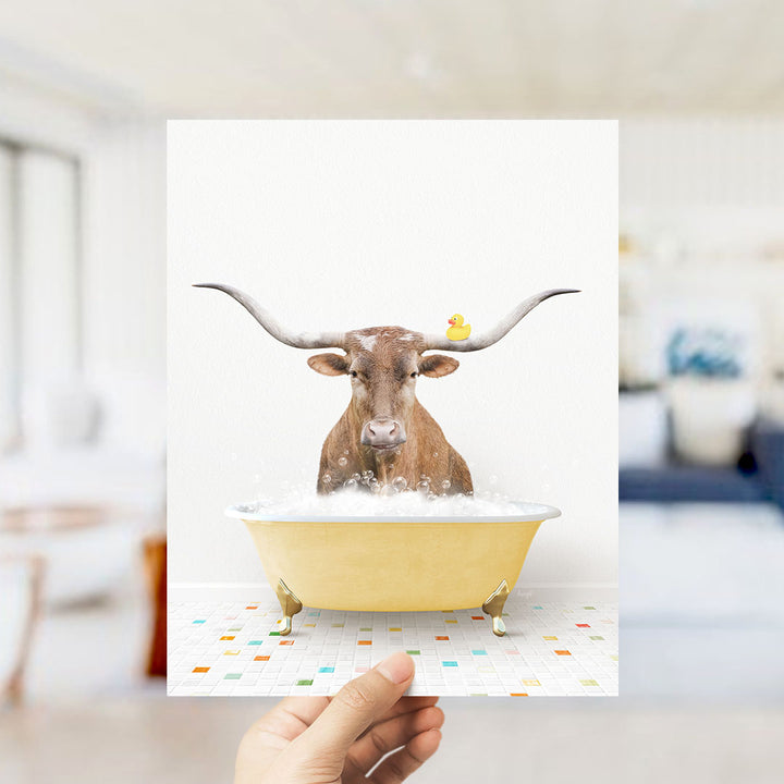 A brown cow with large horns is sitting in a yellow bathtub filled with bubbles, with a yellow rubber duck perched on its head.